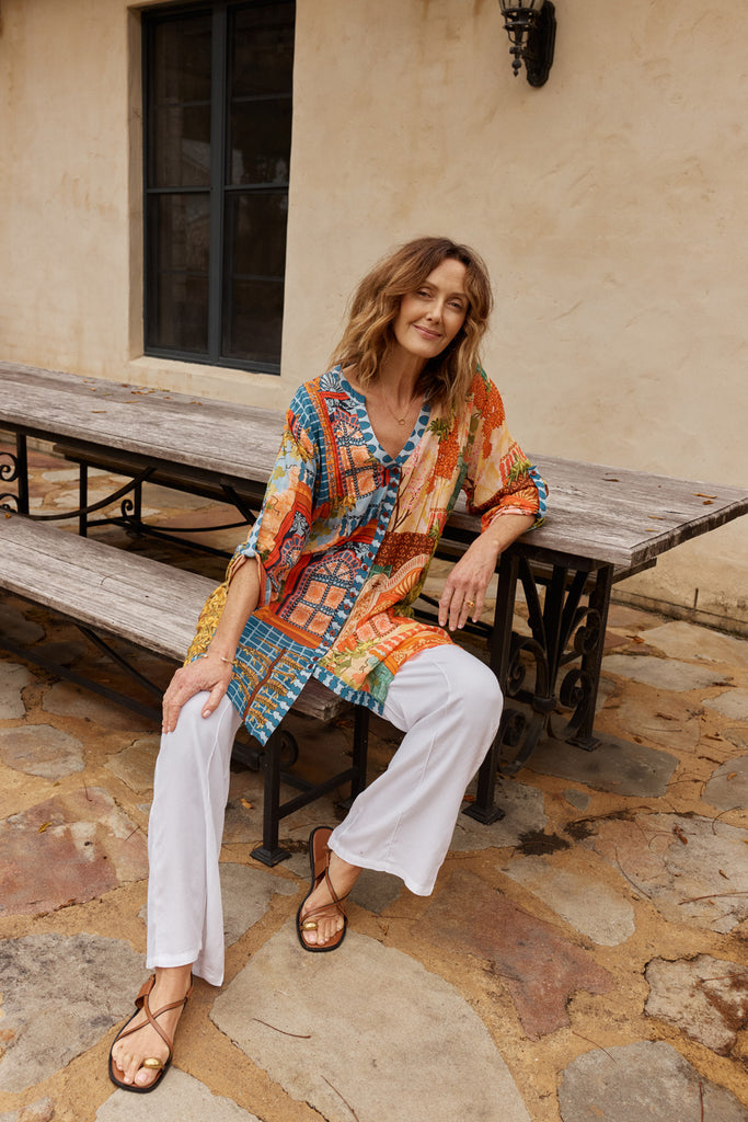 Woman sitting outdoors on a wooden bench wearing the colourful patterned Lulalife Lanthea button dress
